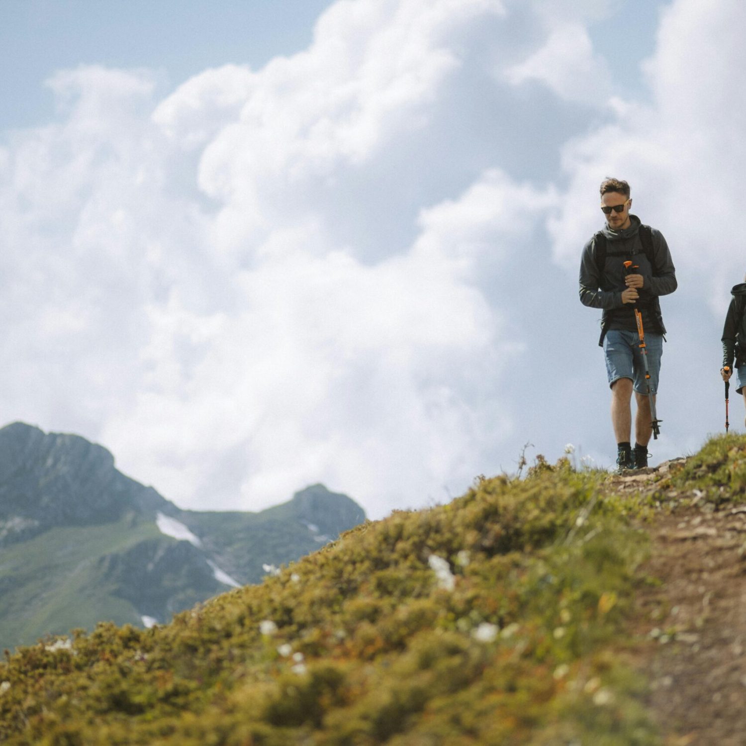 A couple enjoying a hike through lush mountains with trekking poles under a cloudy sky.